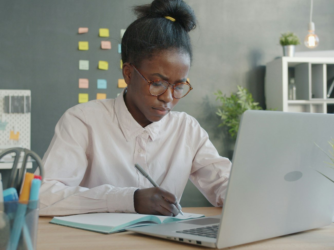 Une jeune femme étudie à un bureau, avec un cahier et un ordinateur portable